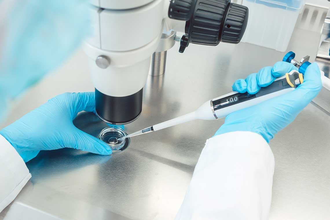 A researcher using a pipette with a sample under a microscope