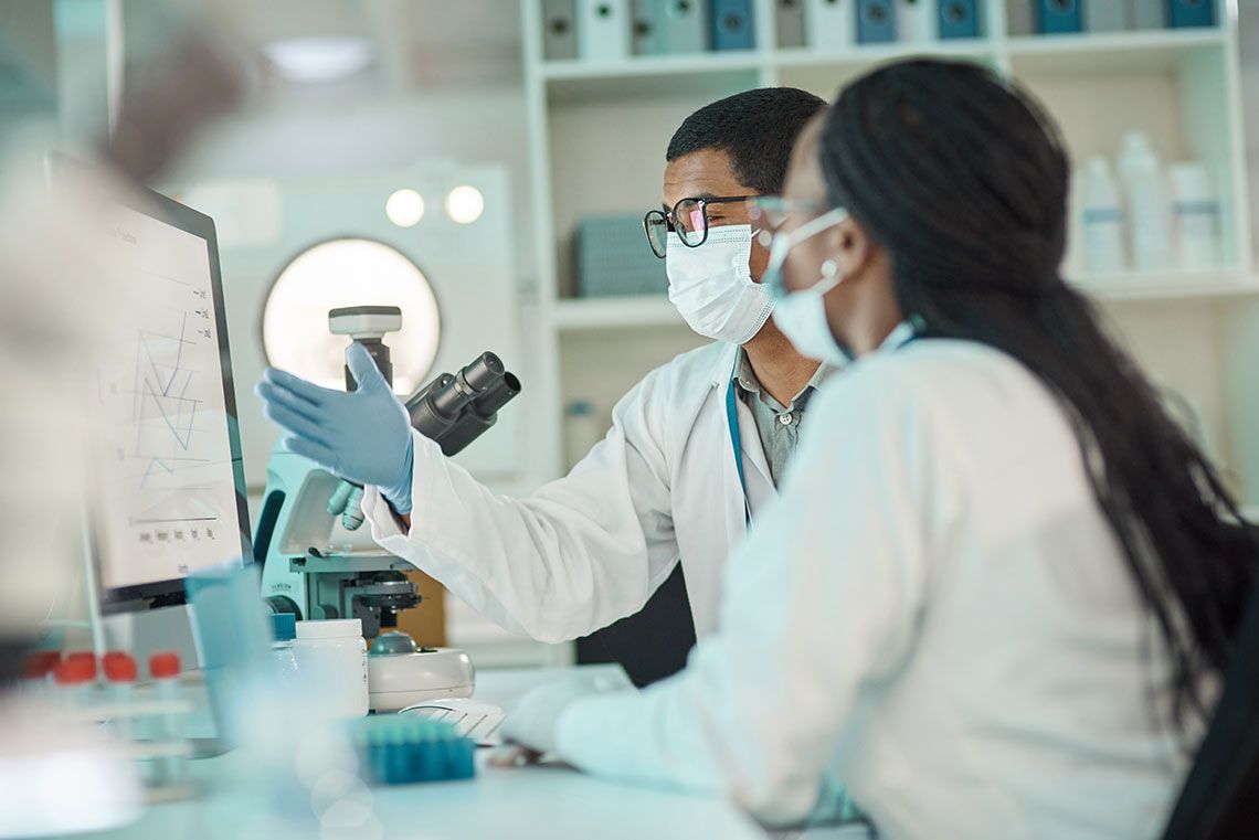 Two researchers at a lab desk wearing masks and gloves