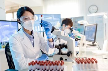 Clinical laboratory technician looking at some sample viles seated in front of a microscope